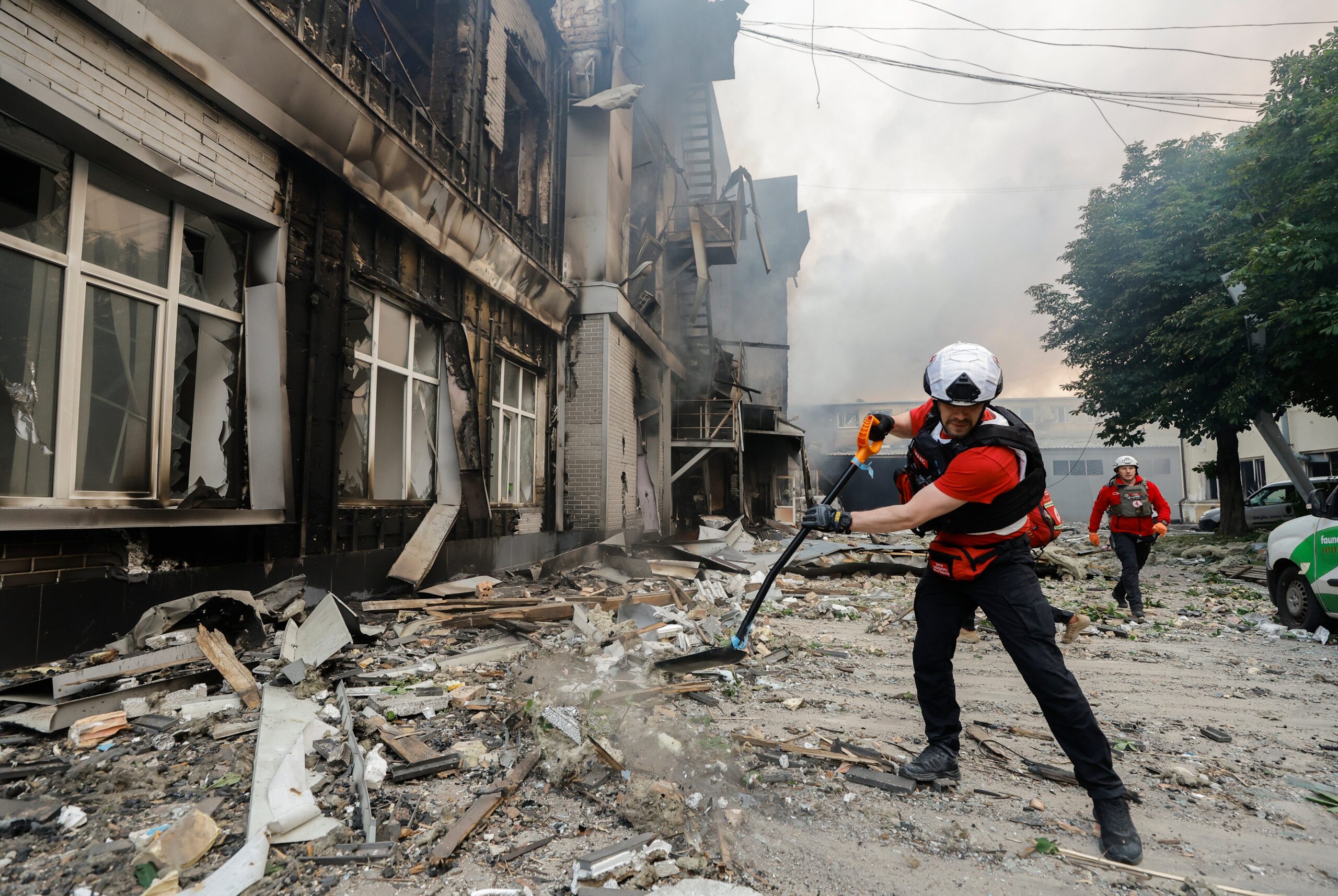 Ukrainian rescuers clean the road for a fire engine at the site of a drone strike