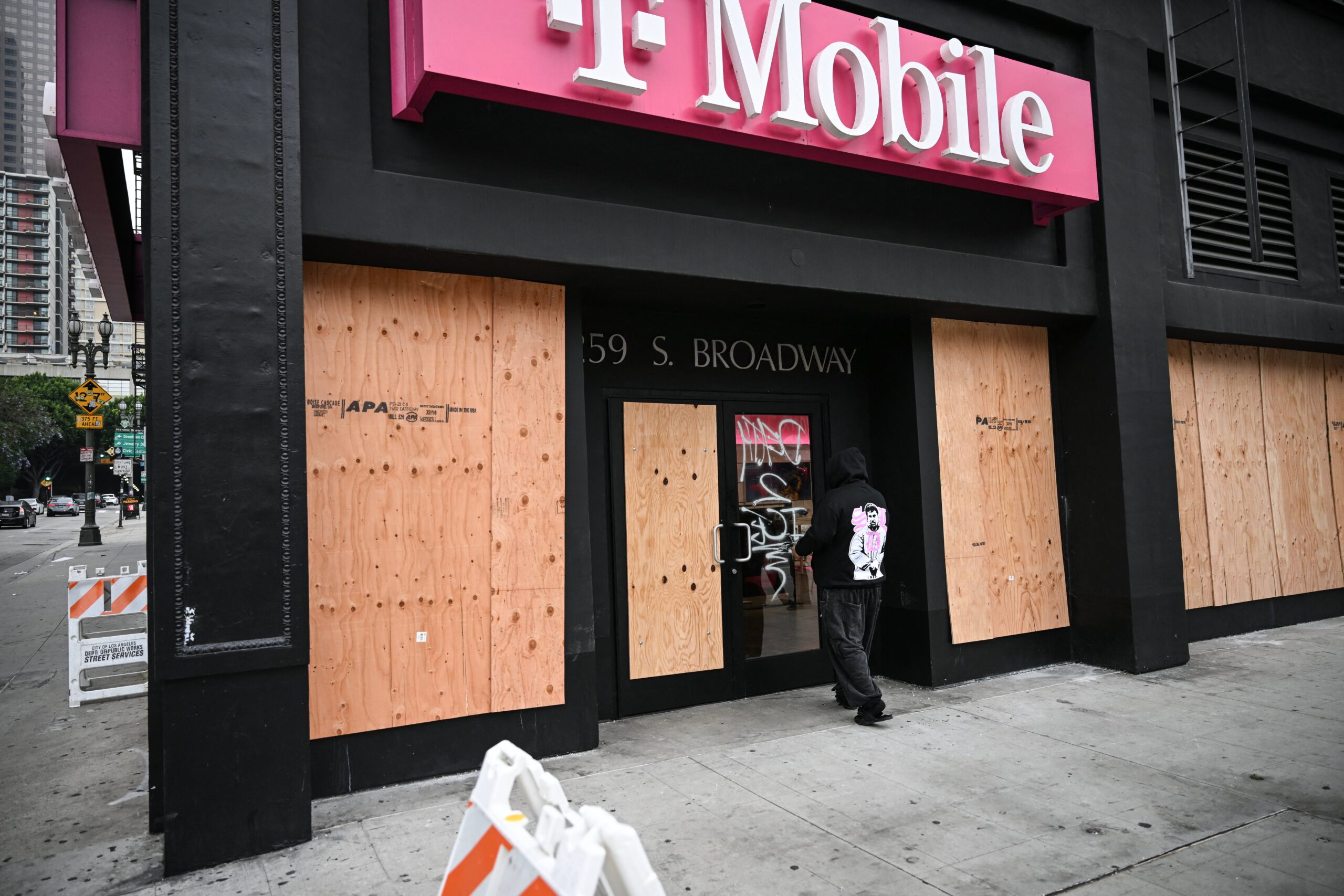 A man walks past a boarded up T-Mobile store that was looted overnight on Sunday