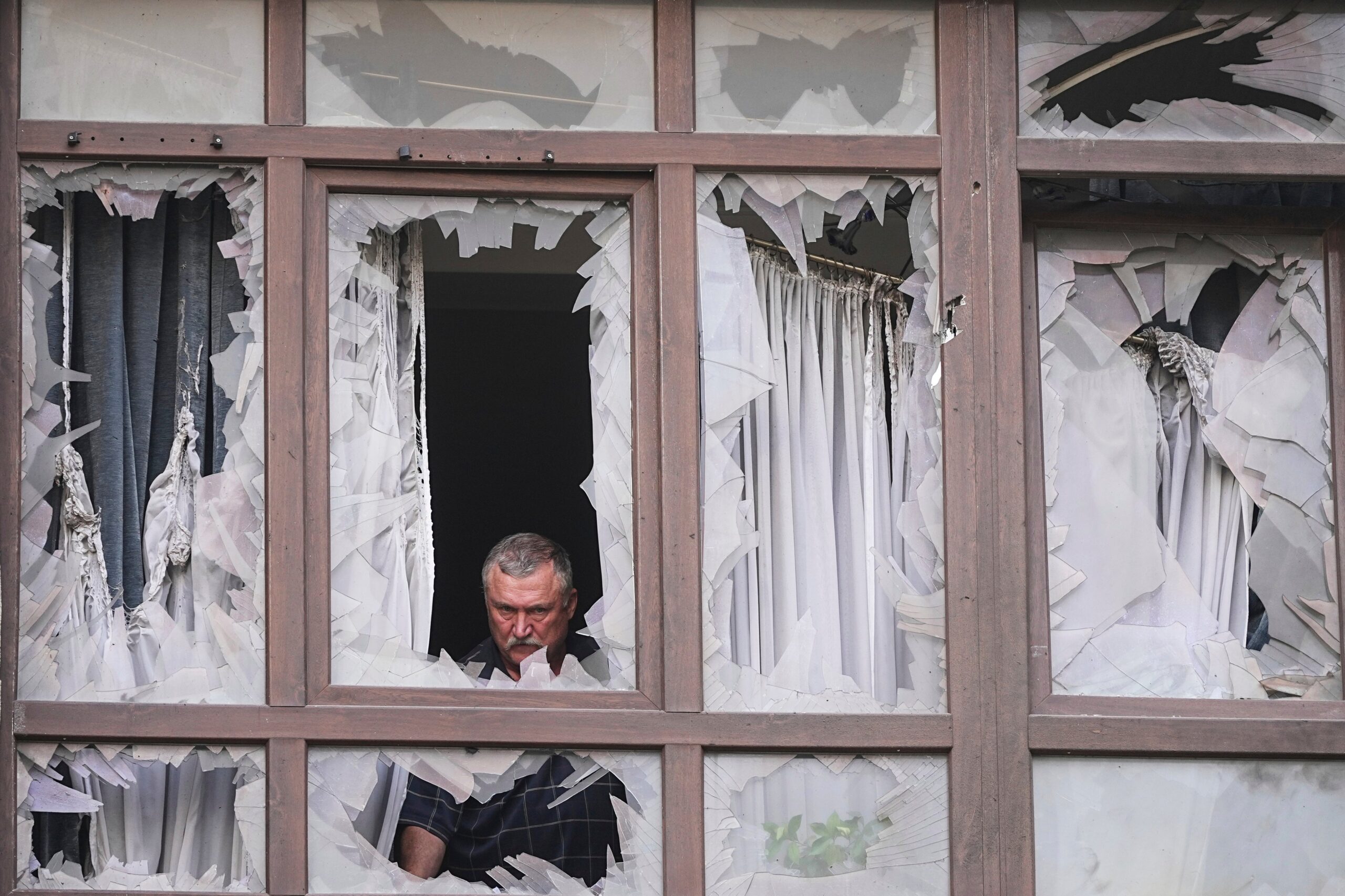 A man stands at the broken windows of his house after a Russian attack in Kyiv