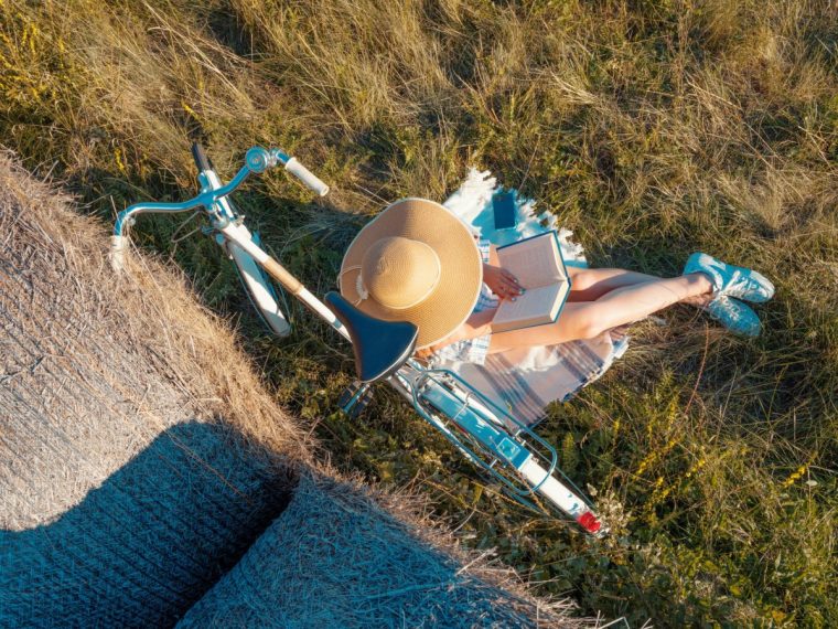 Directly above High angle view of Young Woman with old style bicycle Reading Book While Sitting On Lawn near bale of hay in nature.