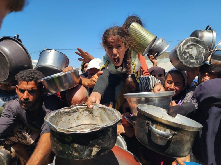KHAN YUNIS, GAZA - JULY 24: Palestinians struggling with hunger crowd around as a charity distributes food in the Al-Mawasi area of Khan Yunis, Gaza amid ongoing Israeli restrictions blocking humanitarian aid from reaching Gaza, on July 24, 2025. (Photo by Hani Alshaer/Anadolu via Getty Images)