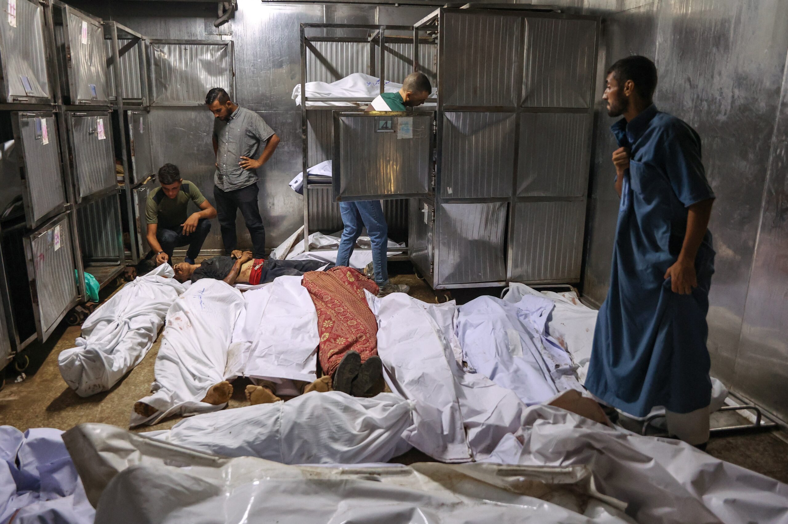 Palestinians mourn over the shrouded bodies of people killed the previous day while seeking aid near Zikim, west of Beit Lahia, in the northern Gaza Strip, at the morgue of at Al-Shifa hospital in Gaza City on August 10, 2025.