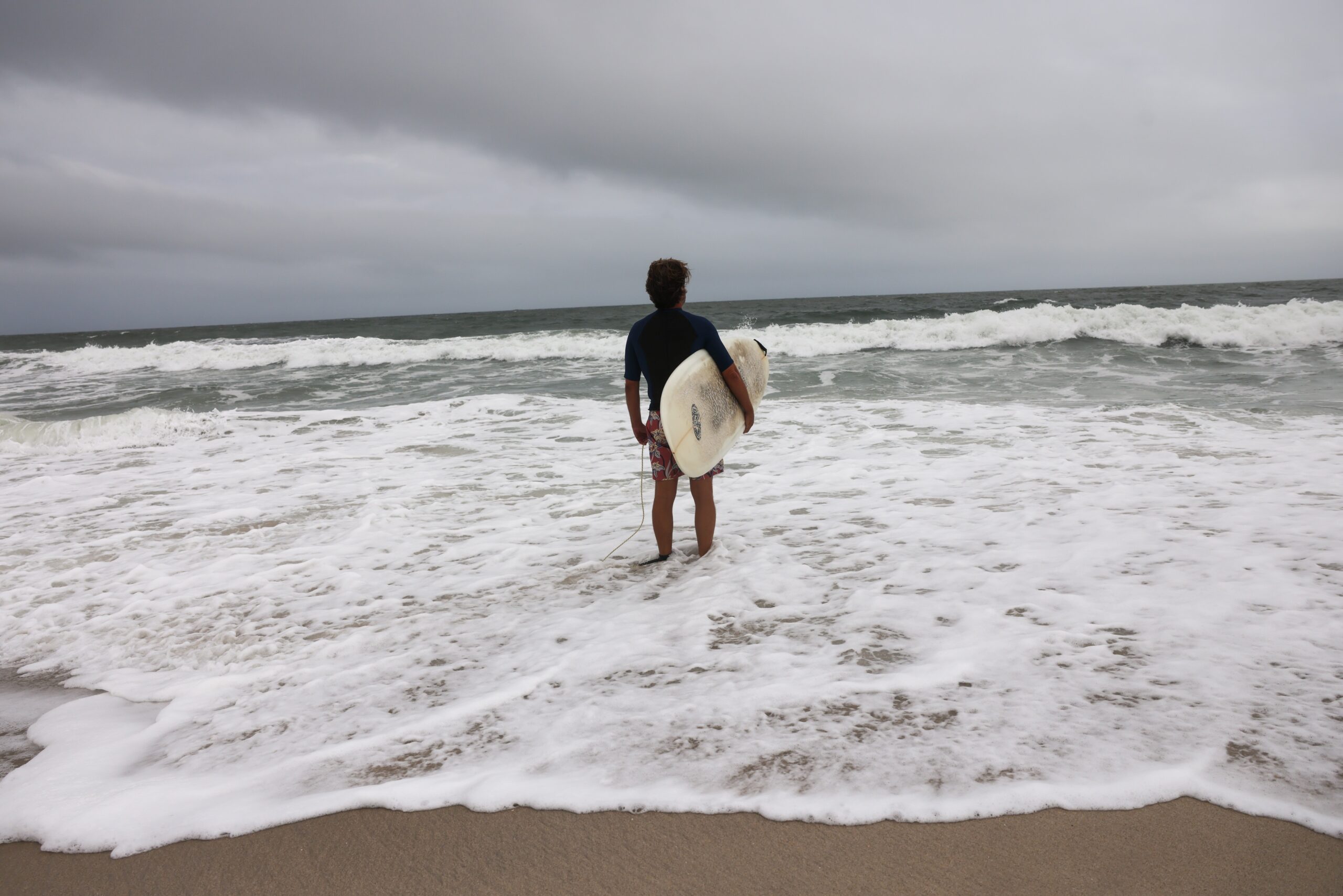 A surfer prepares to go into the ocean on a beach closed to swimmers — there's always one