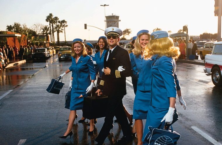 FILM ' Catch Me If You Can' (2003). Picture shows, Leonardo DiCaprio as con man (Frank W Abagnale) posing as a pilot with air hostesses. Photo Credit: Andrew Cooper. Copyright: TM & 2002 DREAMWORKS LLC. Pictured: Passing himself off as an airline pilot, Frank Abagnale (LEONARDO DICAPRIO, center) finds the perfect camouflage - surrounded by a bevy of beautiful stewardesses - in DreamWorks Pictures' CATCH ME IF YOU CAN.
