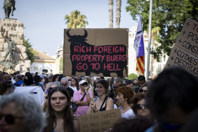 Demonstrators hold signs reading 'Rich foreign property buyers go to hell' during a protest against mass tourism and housing prices in Palma de Mallorca, on the Balearic island of Mallorca on June 15, 2025. (Photo by JAIME REINA / AFP) (Photo by JAIME REINA/AFP via Getty Images)