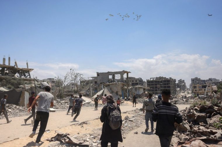 Palestinians in Jabalia in the northern Gaza Strip rush towards a plane conducting an airdrop of aid above the Israel-besieged Palestinian territory on August 1, 2025. US special envoy inspected a US-backed food distribution centre in war-torn Gaza as the UN rights office reported that Israeli forces had killed hundreds of hungry Palestinians waiting for aid. (Photo by Bashar TALEB / AFP) (Photo by BASHAR TALEB/AFP via Getty Images)