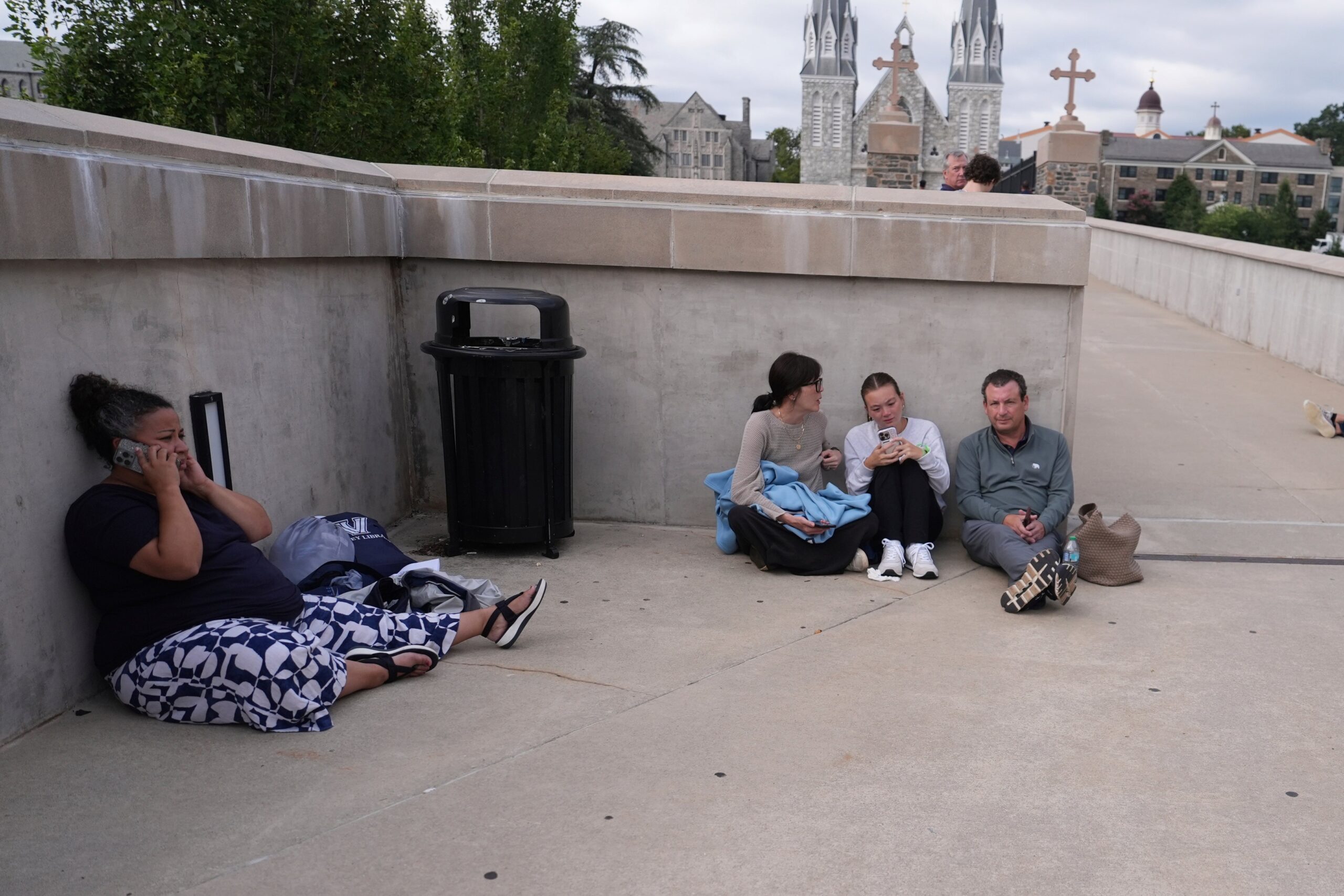 People shelter behind a wall at the Villanova University campus where an active shooter was reported Thursday, Aug. 21, 2025, in Villanova, Pa