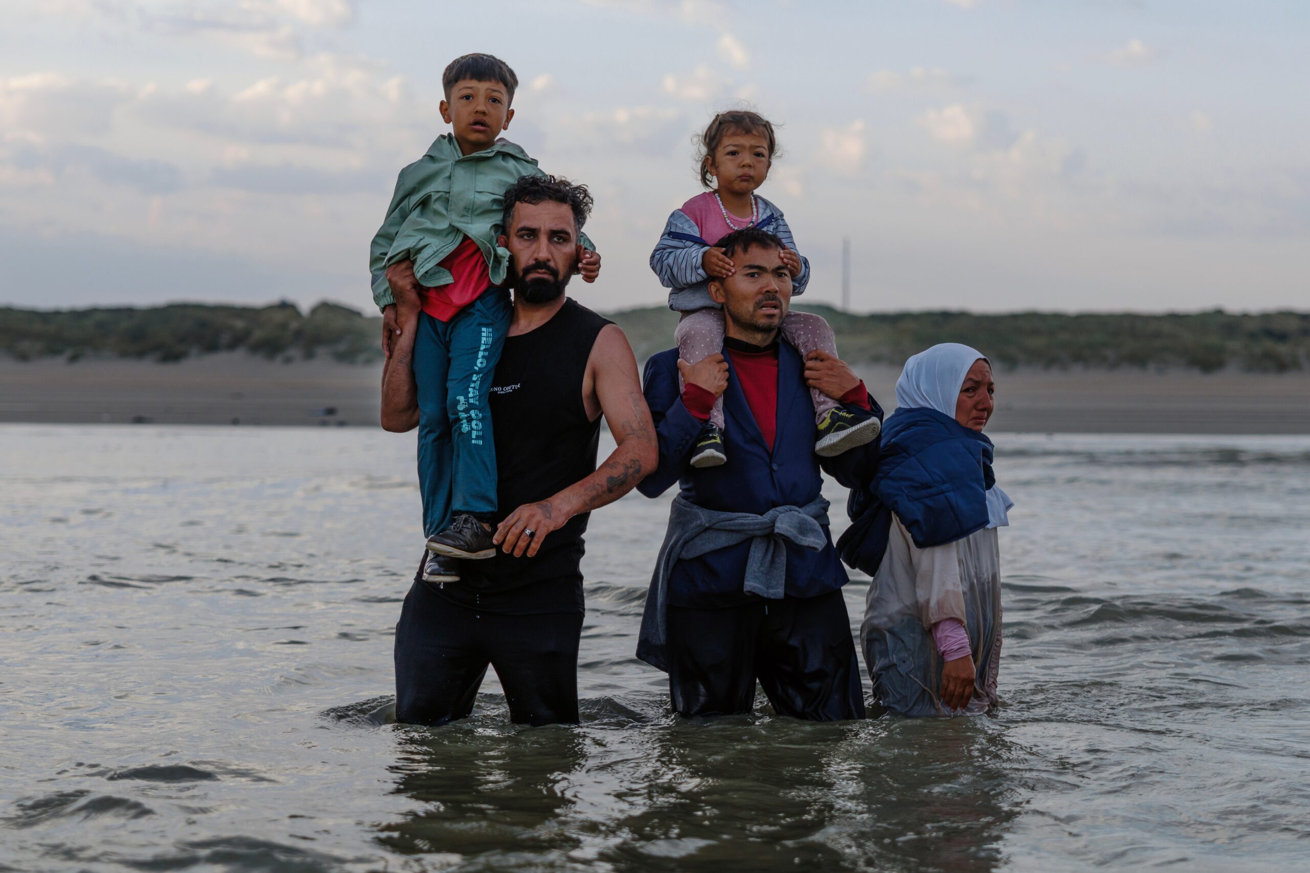 Migrant families stand in the sea dejected after failing to board a small boat on August 12, 2025 in Gravelines, France.