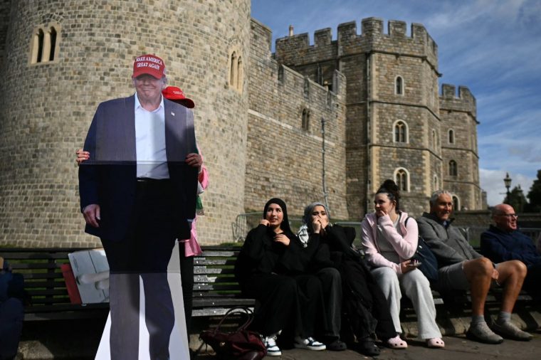 People react as a person holds a cardboard cutout featuring an image of US President Donald Trump wearing a red MAGA cup, outside Windsor Castle in Windsor, on September 16, 2025, on the eve of a State Visit by the US President and the First Lady. Donald Trump lands in Britain on Tuesday for an historic second state visit that will see the UK government spare no effort in trying to flatter the mercurial American president. (Photo by JUSTIN TALLIS / AFP) (Photo by JUSTIN TALLIS/AFP via Getty Images)