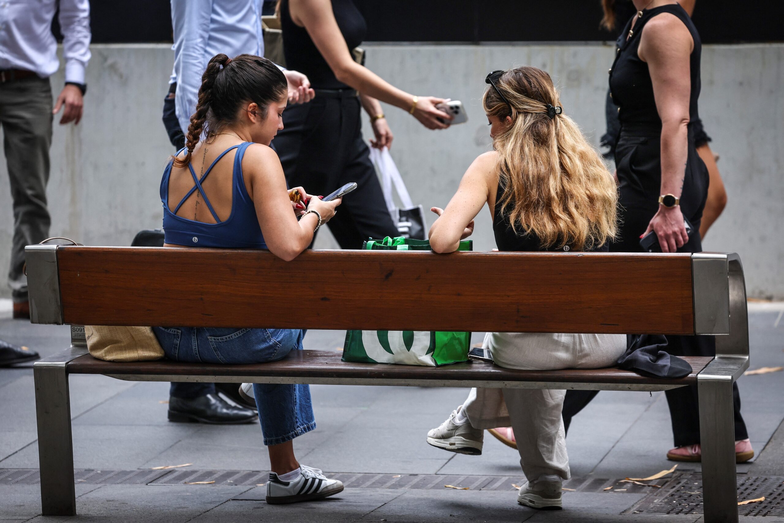 Two women sitting on a bench look at their phones in central Sydney