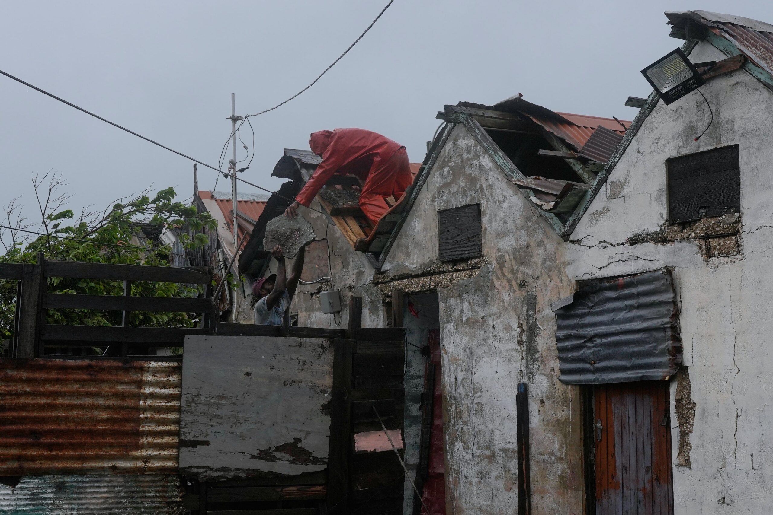Men remove a loose section of roof in Kingston, Jamaica, as Hurricane Melissa approaches