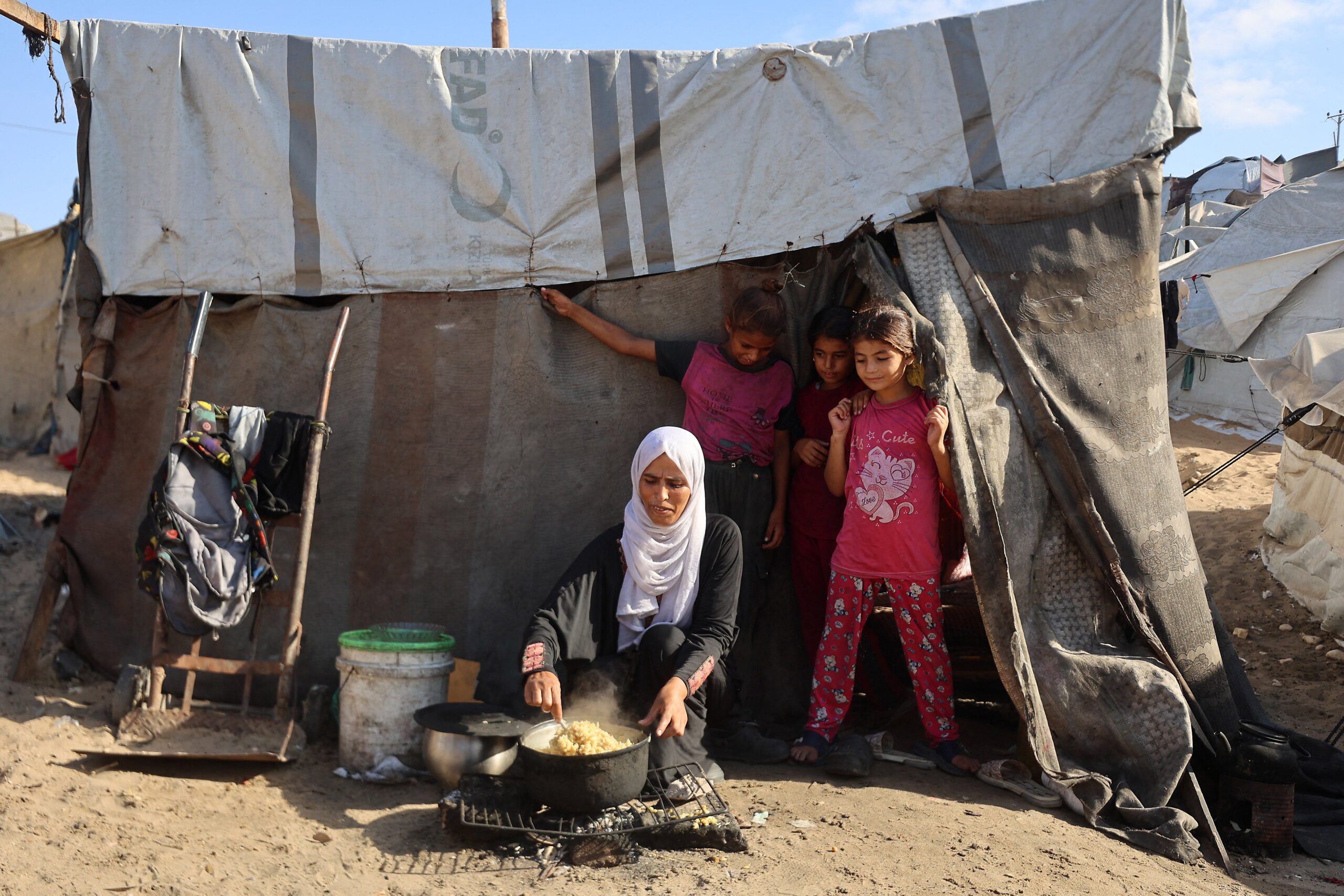 A Palestinian woman cooks next to children in front of a tent at a camp for displaced people in Khan Yunis in the southern Gaza Strip, on 29 September 2025