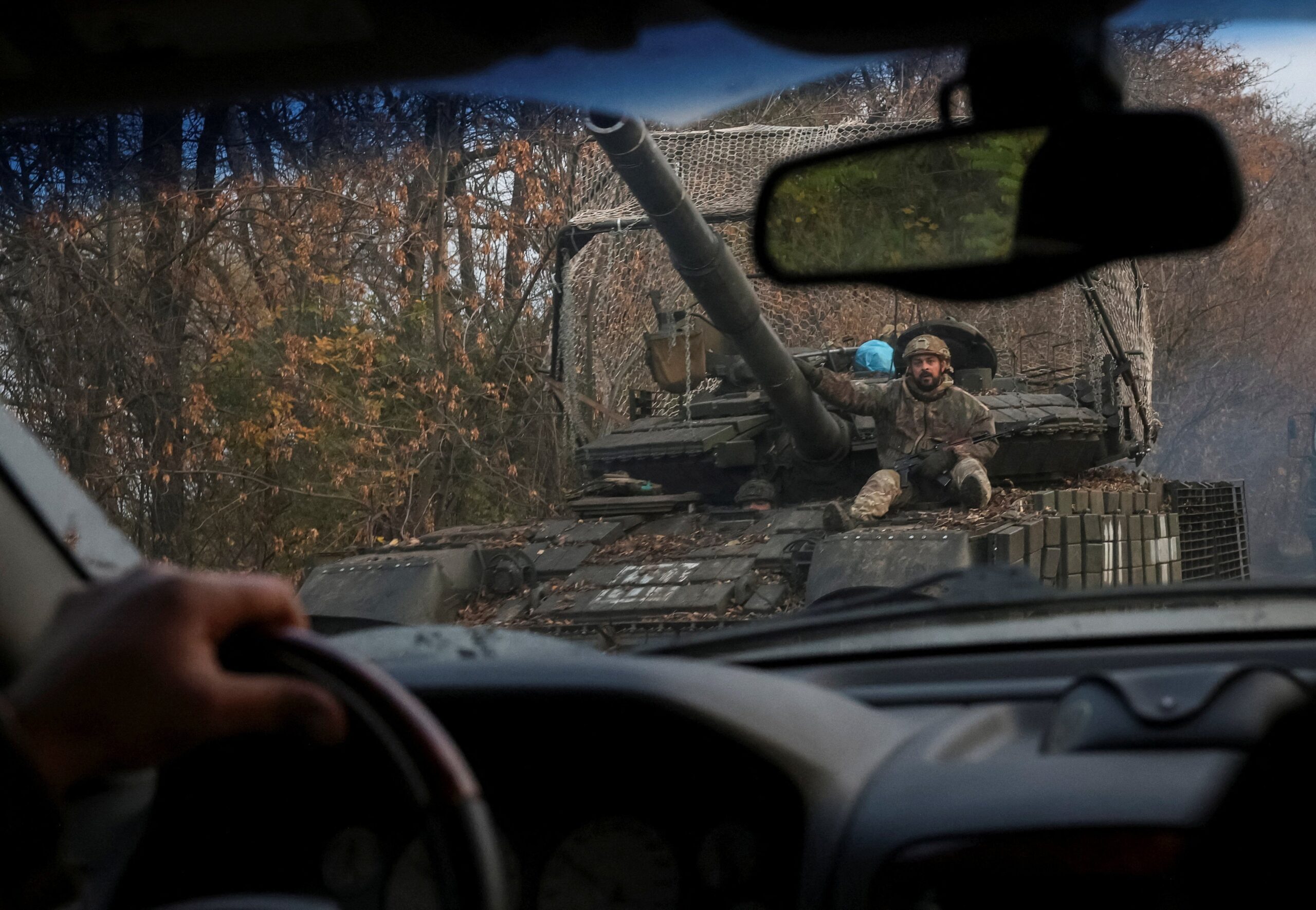 Ukrainian servicemen ride a tank, as seen through a car windshield