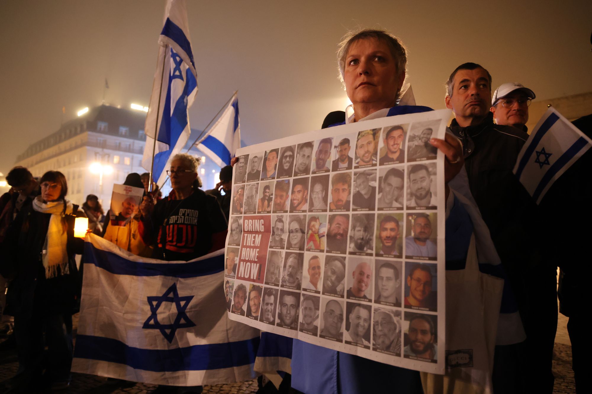 People, including one woman holding a placard showing hostages still held by Hamas, gather in the early hours at the Brandenburg Gate to read out the names of victims of the 7 October 2023 attack by Hamas in Israel on the second anniversary in Berlin, Germany