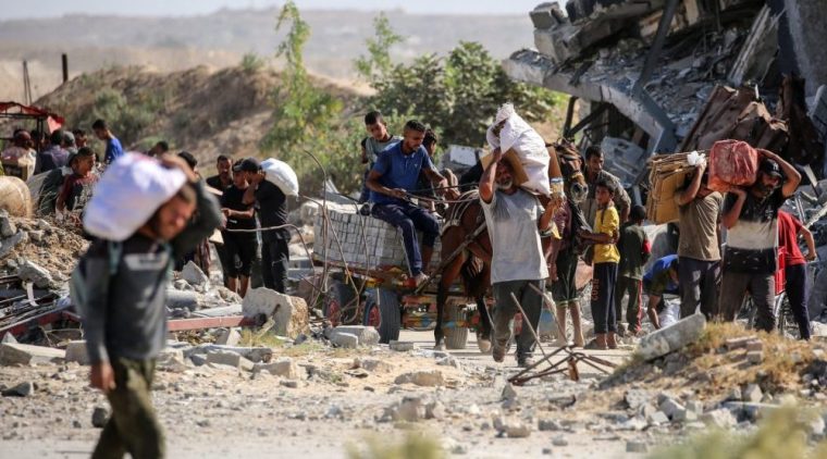 Palestinians carrying bags and empty cardboard boxes walk past a destroyed building asthey return from a food distribution point run by the US and Israeli-backed Gaza Humanitarian Foundation (GHF) group, near the Netsarim corridor in the central Gaza Strip on October 5, 2025. A senior Hamas official on October 5 said the Palestinian militant group is eager to reach an agreement to end the war and implement a prisoner swap with Israel, as negotiators converge in Egypt for talks. (Photo by Eyad BABA / AFP) (Photo by EYAD BABA/AFP via Getty Images)