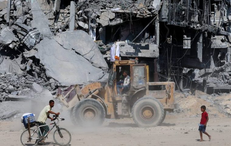 Palestinians pass by rubble, amid a ceasefire between Israel and Hamas in Gaza, in Khan Younis, in the southern Gaza Strip, October 14, 2025. REUTERS/Ramadan Abed
