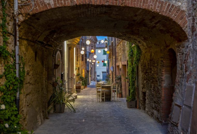 Italy, Province of Siena, Radicondoli, Lanterns illuminating old town alley with brick arch in foreground