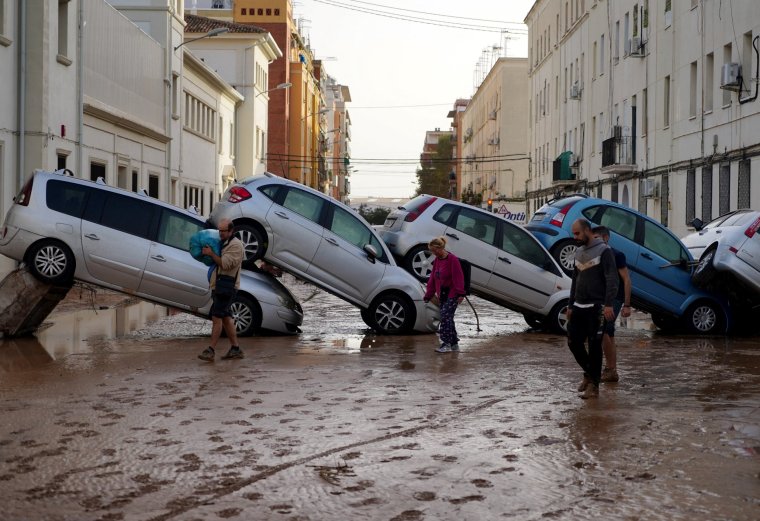 (FILES) Residents walk past piled up cars following deadly floods in Valencia's De La Torre neighbourhood, south of Valencia, eastern Spain, on October 30, 2024. One year ago 237 people were killed in Spain'sworst natural disaster in a generation. The floods hit 78 municipalities, sweeping away 130,000 vehicles and damaging thousands of homes, generating 800,000 tonnes of debris, mainly around Valencia, Spain's third-largest city. (Photo by Manaure QUINTERO / AFP) (Photo by MANAURE QUINTERO/AFP via Getty Images)