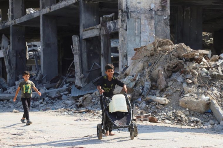 Displaced Palestinian children walk, as one of them moves a cart loaded with water containers, amid a ceasefire between Israel and Hamas, in Gaza City, October 19, 2025. REUTERS/Ebrahim Hajjaj