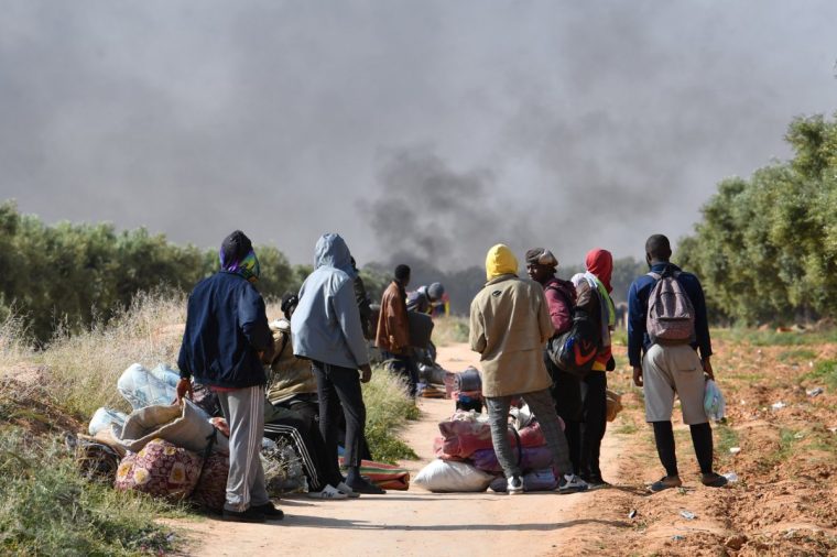 TOPSHOT - Migrants leave with their belongings from a camp for undocumented migrants from sub-Saharan Africa at al-Amra on the outskirts of the Tunisian port city of Sfax on April 5, 2025, after authorities started dismantling the camp. Tunisia on Friday dismantled camps housing thousands of undocumented migrants from sub-Saharan Africa, police said, following a campaign against them on social media. Around 20,000 migrants had set up tents in fields in the eastern regions of El Amra and Jebeniana, national guard spokesman Houcem Eddine Jebabli told AFP. (Photo by FETHI BELAID / AFP) (Photo by FETHI BELAID/AFP via Getty Images)