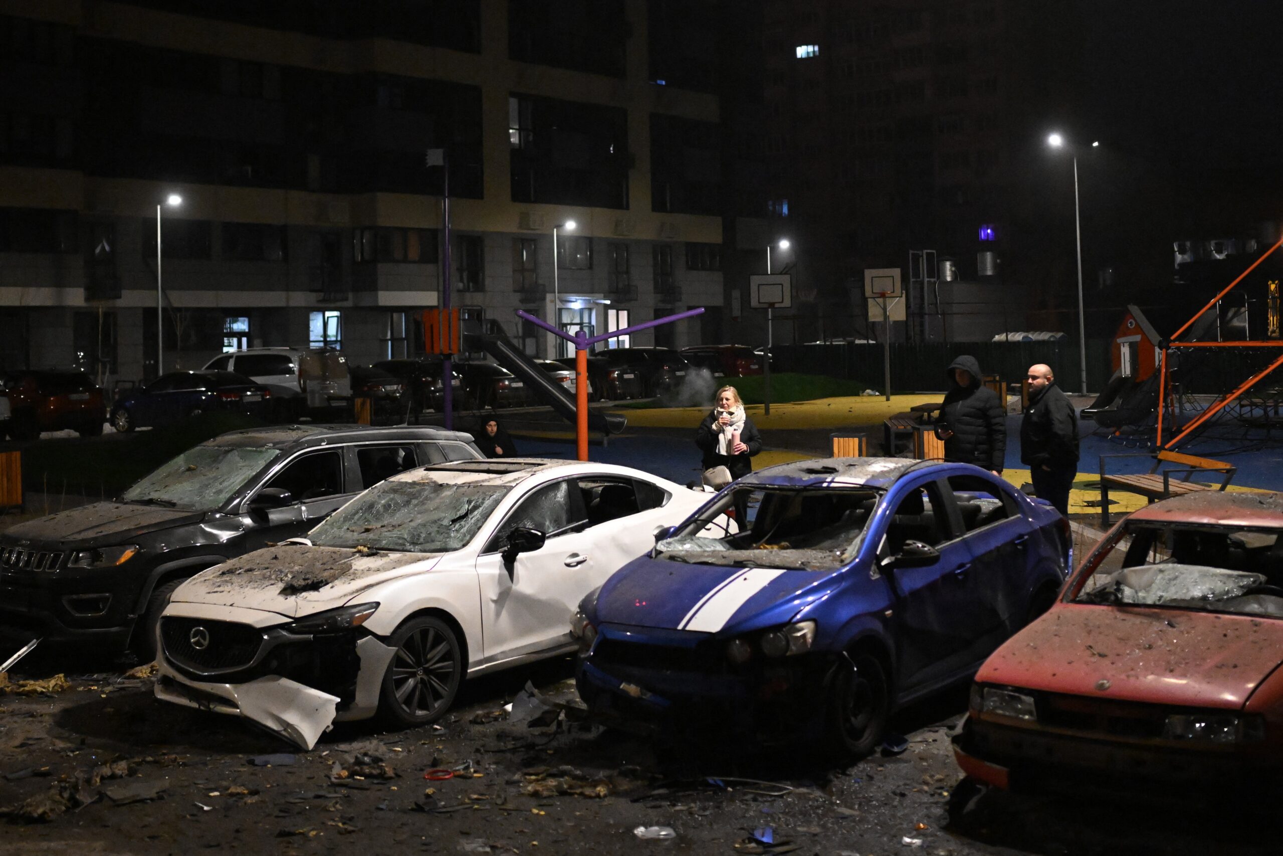Local residents stand next to damaged cars