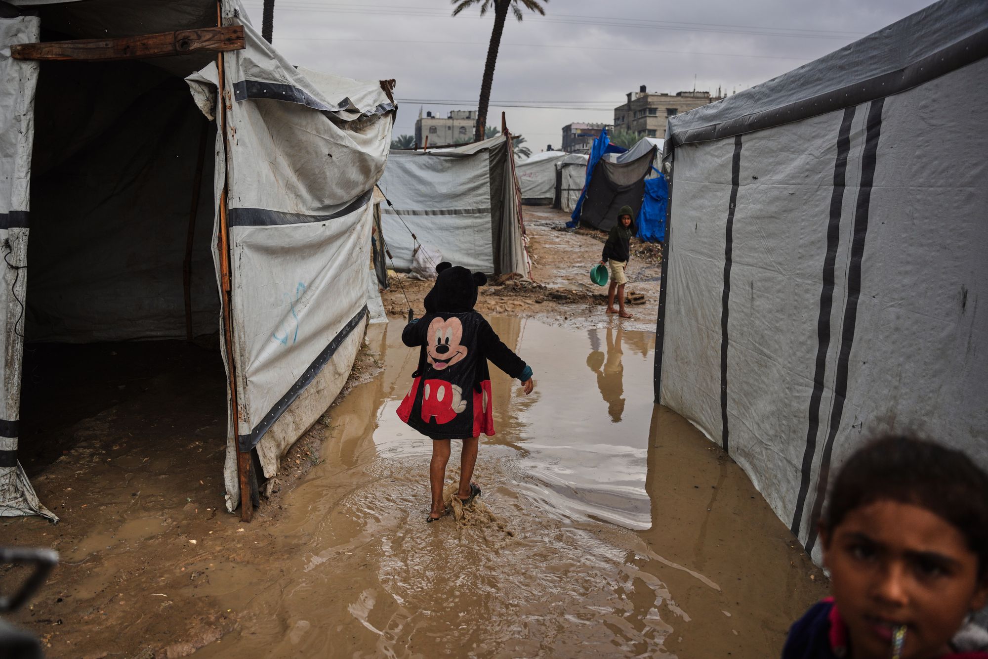 A Palestinian walks through a mud puddle at a temporary tent encampment flooded by a heavy rainfall in Deir al-Balah, central Gaza Strip