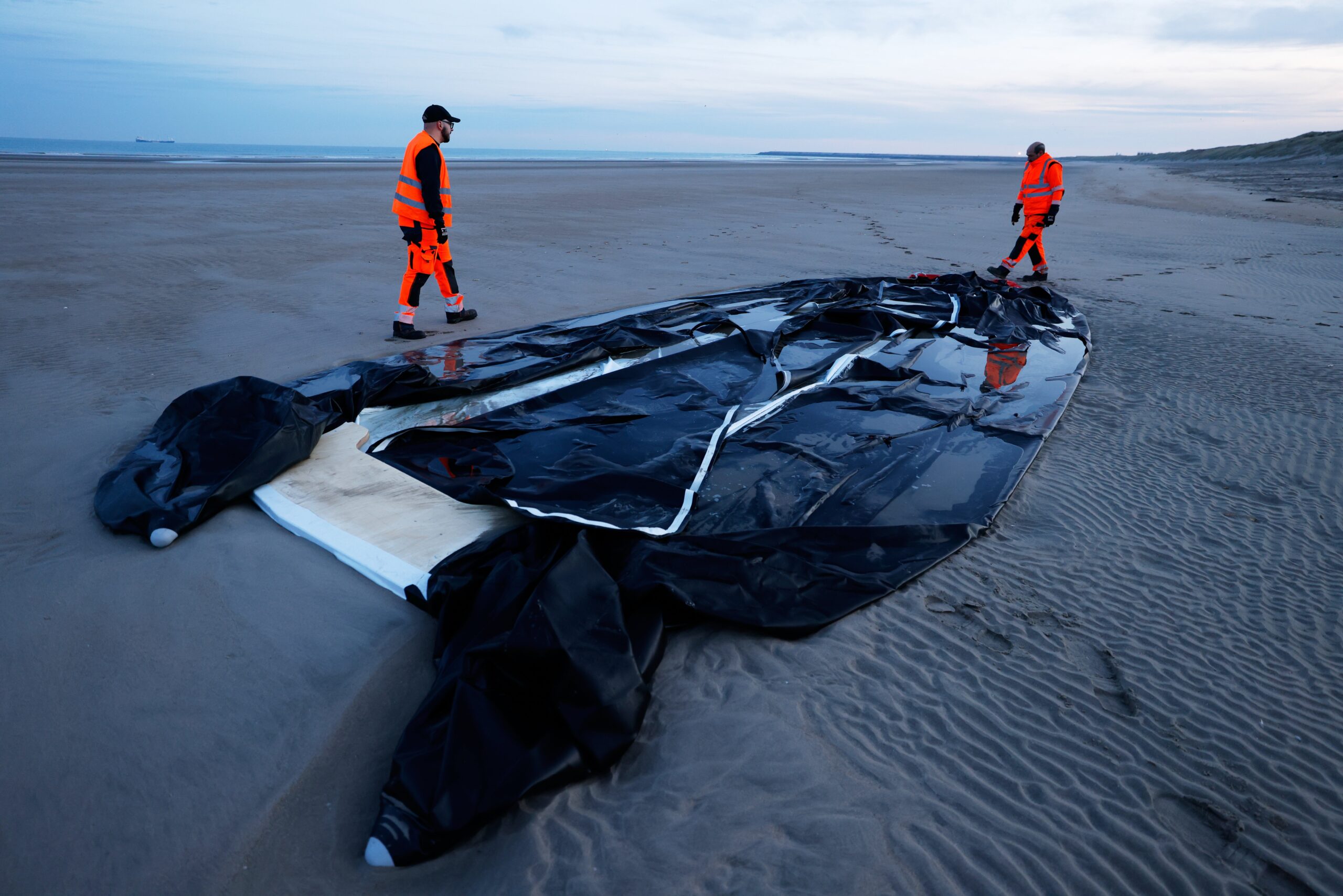 Town employees walk next to an inflatable boat punctured by French police and used by migrants to cross the Channel