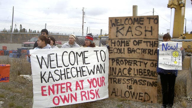 An undated photo shows residents holding signs calling for improved conditions at the Kashechewan First Nations Reserve in Ontario